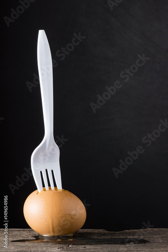 white plastic fork stabbing eggshell the raw egg is overflow, about food concept