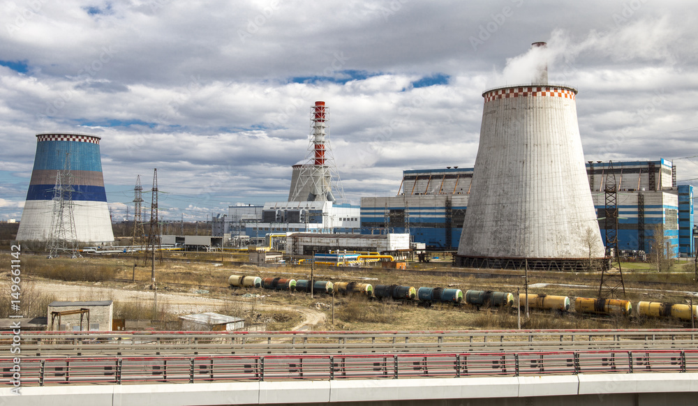Heat and electricity power station. Cooling towers working. Road infrastructure in foreground. Railroad tanks moving from station.