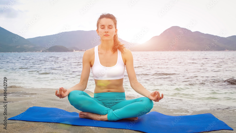 Young woman practicing yoga on the beach at sunset. Lotus pose