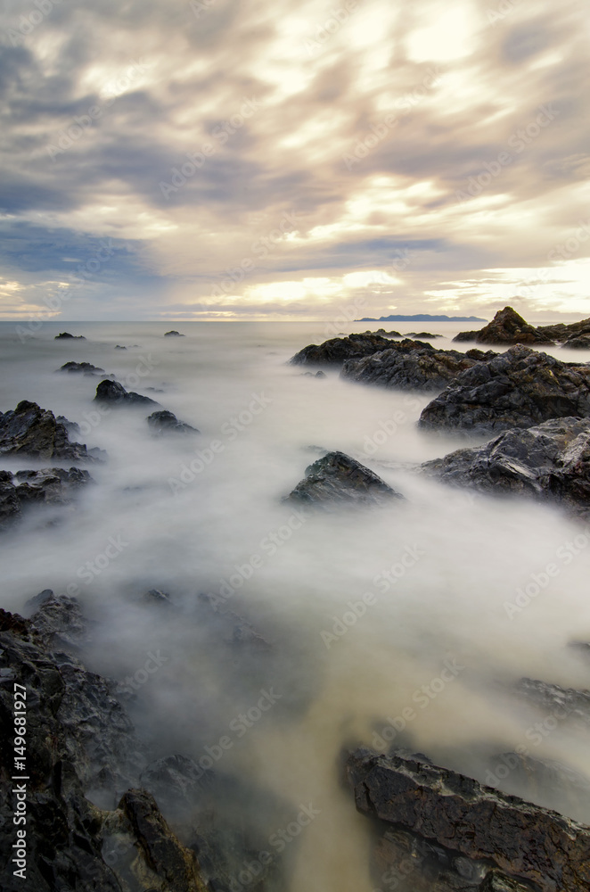 mystical sunrise moment near the sea shore with cloudy sky.soft wave hitting the sandy beach due to long exposure.