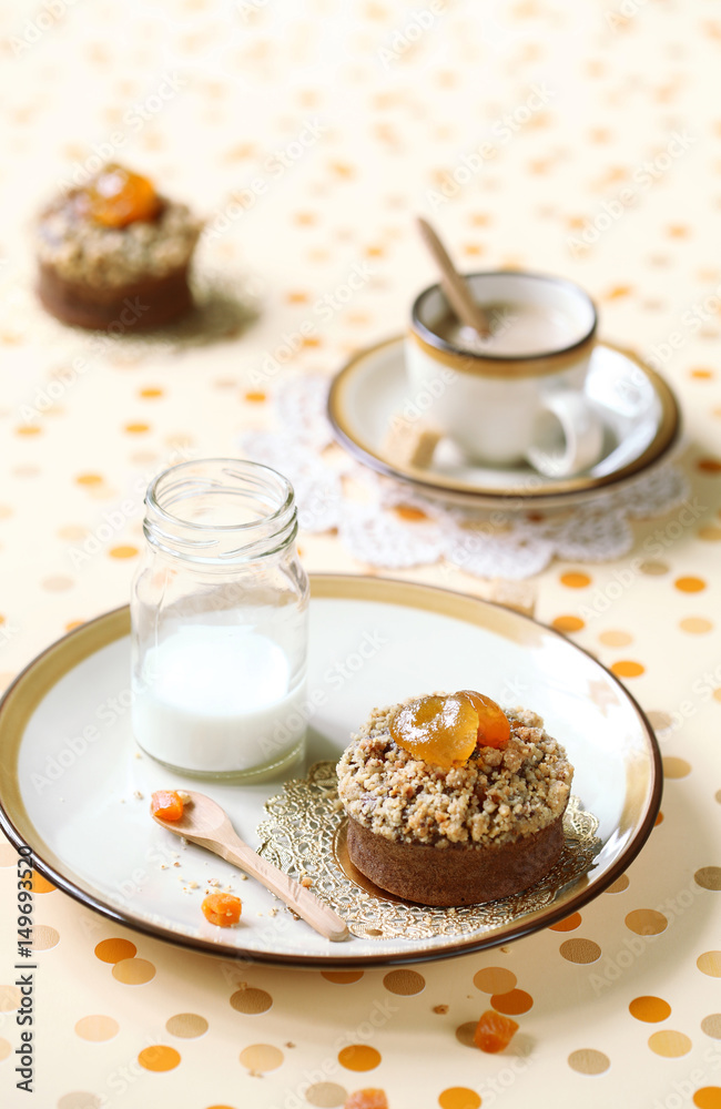 Chocolate Financier Cake with Apricots and Streusel Topping on plate, little bottle of milk and cup of coffee, on bright polka dotted background.