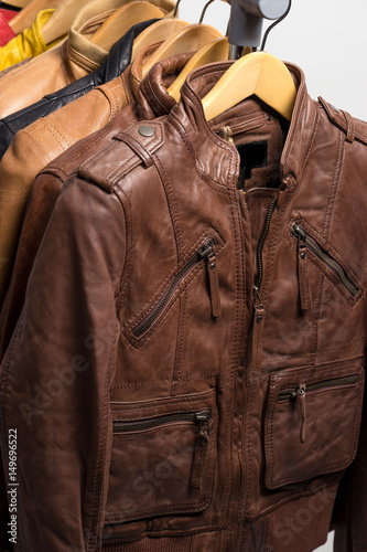 Different color leather jacket hanging on rack on white background