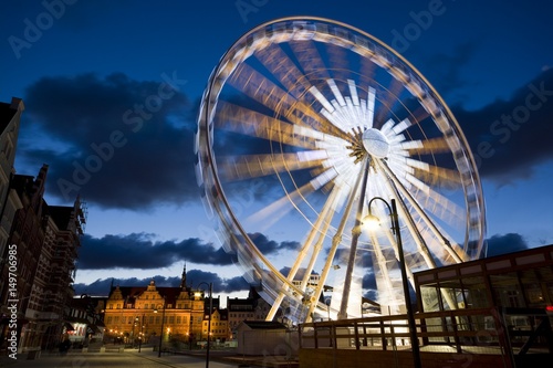 Rotating Ferris wheel located in the Old Town of Gdansk, Poland at night. Green Gate in the background