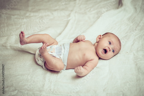 happy baby lying on white sheet and holding his legs