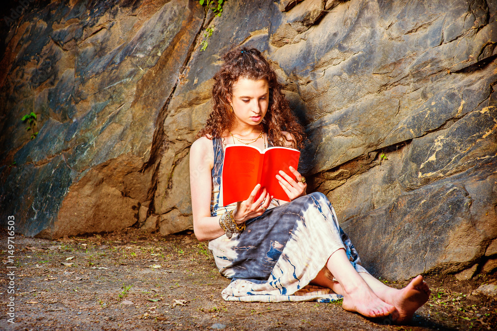 Young American Woman reading red book, sitting on ground, traveling in New York in summer