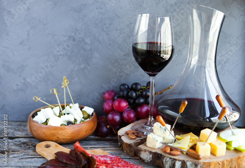 Wine snack set. Glass of red wine, grape, cheese, over rustic wooden background.