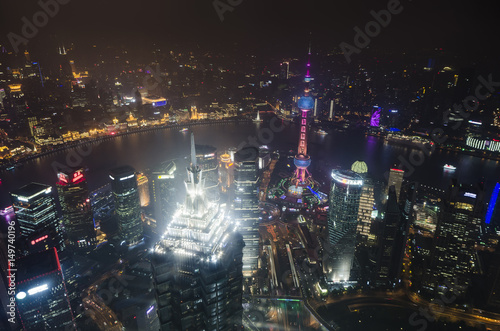 Shanghai's imposing skyscrapers at night with the Bund and downtown skyline across Huangpu river. Beautiful bright night scape lights and clear aerial sky view in Pudong district, Shanghai China, Asia
