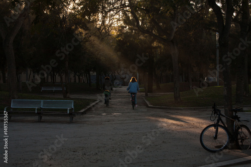 Sun shining through the trees two girls passing on a bike