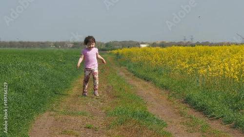 Little girl runs in the meadow. The child runs on a country road. A happy child runs in yellow flowers. Rapeseed field. photo