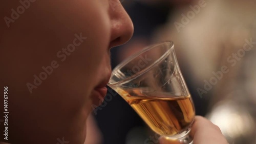 Girl drinks whiskey from a small glass in a bar. Blonde girl tasting cognac in bar