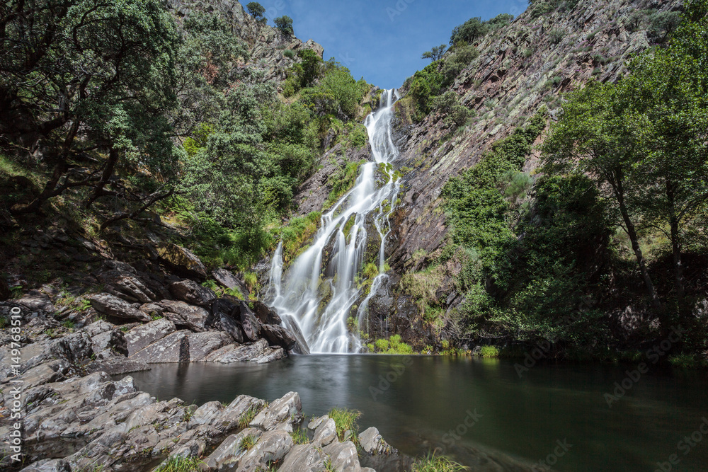 Long exposure of a waterfall with rocks and green during a sunny day