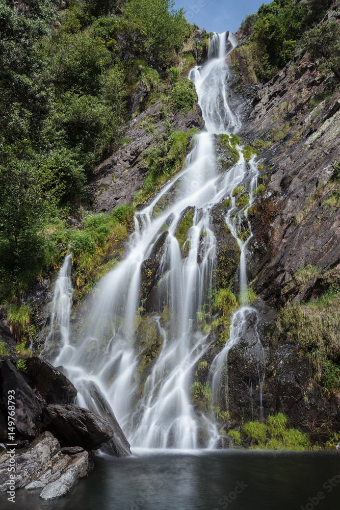 Long exposure of a waterfall with rocks and green during a sunny day