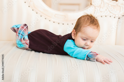 Adorable baby boy with red hair and blue eyes. Newborn child lyling in couch.