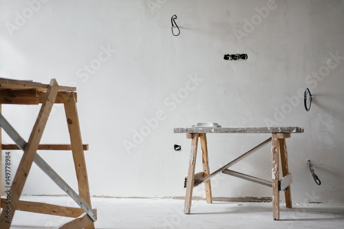 Repair in the apartment. Construction grunge ladder in white interior, of a bright room with fresh plastered walls. White walls in a building construction house.