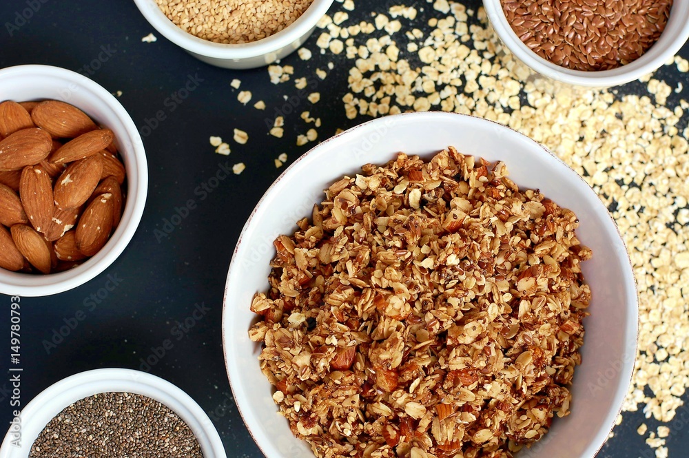 Homemade granola in white bowl with almond and seeds on black background Homemade granola in white bowl with almond and seeds on black background