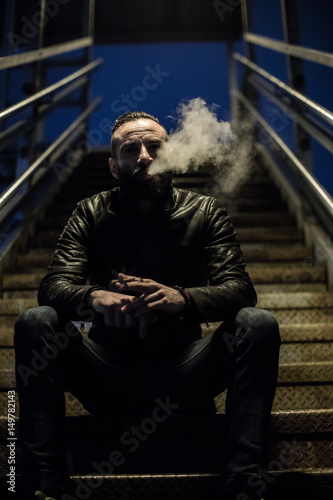 A well groomed, hipster smokes in the streets of Brooklyn. He stands alone under a streetlight during the Spring of 2017.