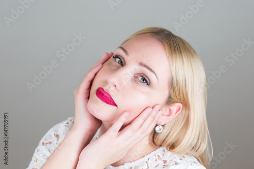 Young blonde woman holds hands on face