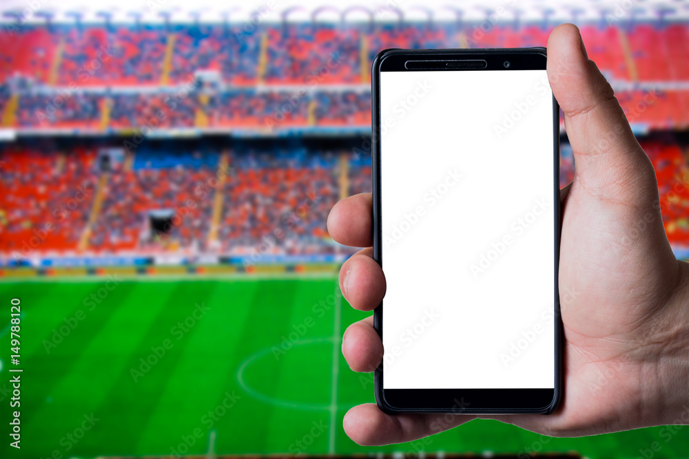 Mans hand holding a smartphone against soccer or football background.