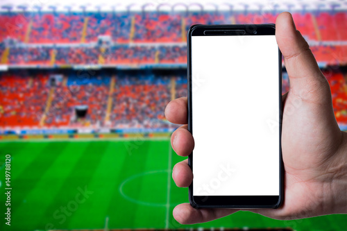 Mans hand holding a smartphone against soccer or football background.