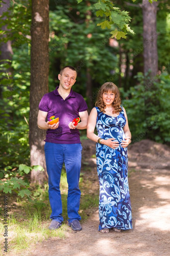Fototapeta premium Portrait of a caucasian pregnant woman and her husband holding toys for baby outdoors