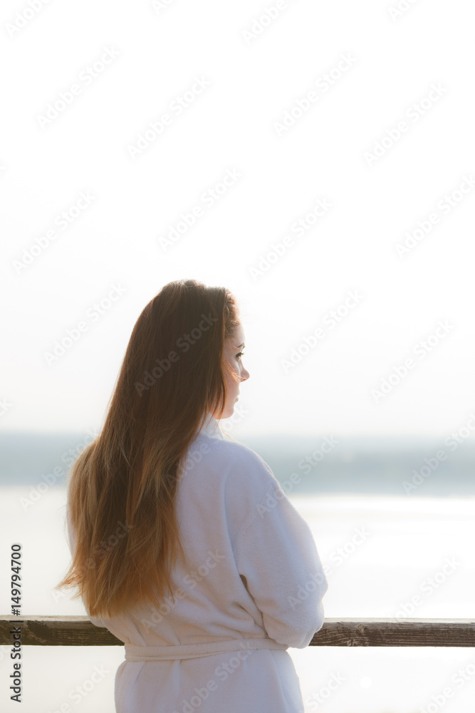 The girl is standing in the bathrobe in the sun