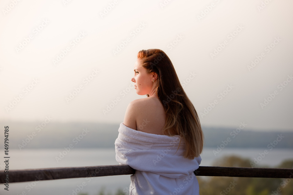 The girl is standing in the bathrobe in the sun