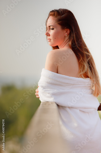 The girl is standing in the bathrobe in the sun