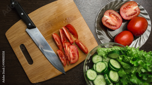 tomato and cut tomato, cucumber and a kitchen knife on a cutting board