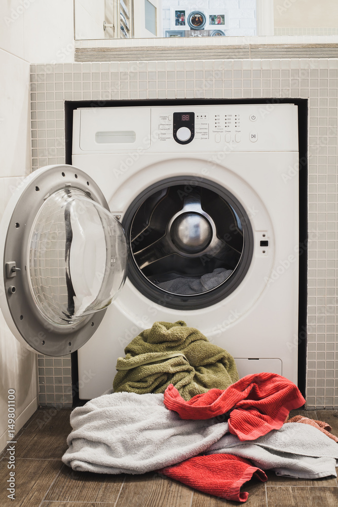 Washing machine with multicolored dirty towels on the floor near it. laundry washer with opened door. Frontal view. Vertical Washing machine with multicolored dirty towels on the floor near it. laundry washer with opened door. Frontal view. Vertical