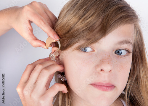 Audiologist fitting a hearing aid to an adorable young girl patient