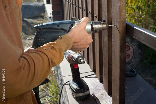 Man hands drilling wooden fence to metal construction. Building a wooden fence with a drill and screw. Close up of his hand and the tool in a DIY concept.