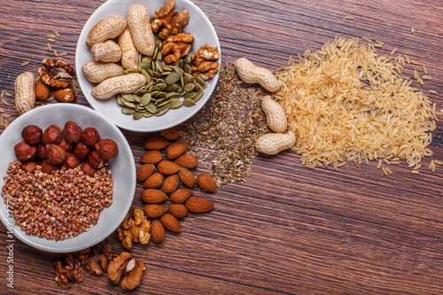 Assorted nuts in white bowl, plate on wooden surface. Top view with copy space