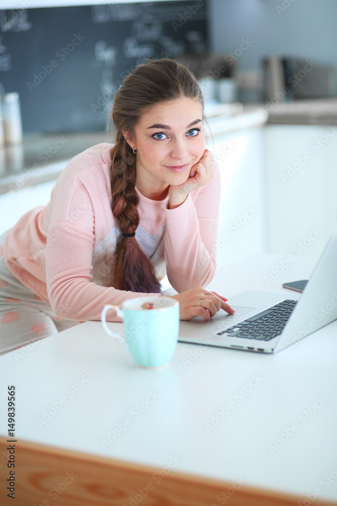 Young woman standing in kitchen using laptop