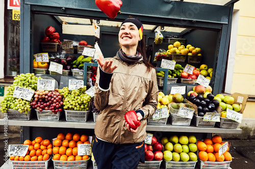 Smiling young woman tosses red pepper while standing against stall