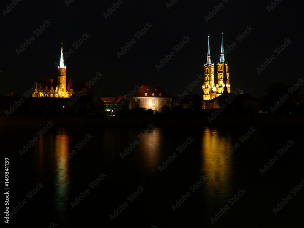 Ostrow Tumski at night. Illuminated town house and collegiate church. Gothic cathedral on Tumski island. Wroclaw and one of the famous landmarks in the city. Reflection in the Odra River. Poland
