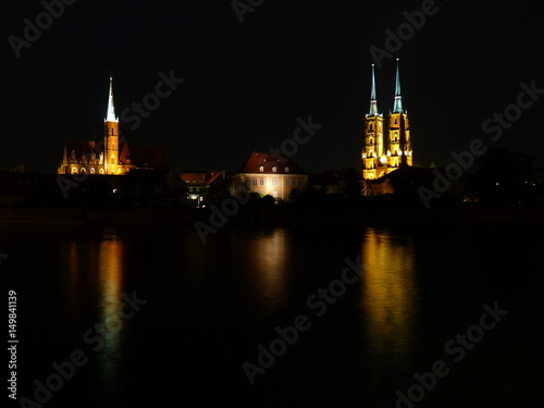 Ostrow Tumski at night. Illuminated town house and collegiate church. Gothic cathedral on Tumski island. Wroclaw and one of the famous landmarks in the city. Reflection in the Odra River. Poland