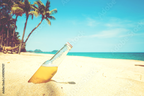 Fototapeta Naklejka Na Ścianę i Meble -  Beer bottle on a sandy beach with palm tree. vintage color tone effect