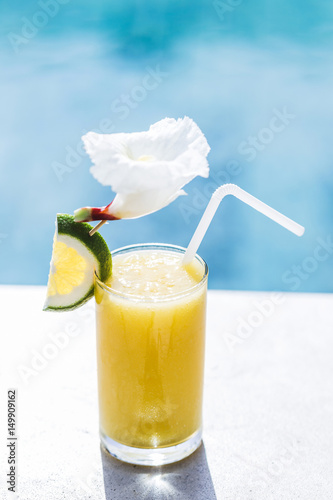 Fresh cold fruit juice on poolside. With straw, slice of lime and tropical flower