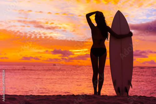Hawaii surfer woman at sunset with surfboard on beach. Surf lifestyle.