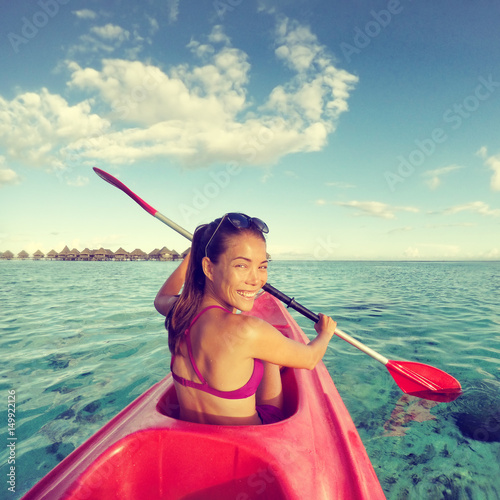 Kayak woman having fun kayaking at tropical beach resort in Tahiti vacation travel. Asian girl enjoying watersport on holidays at sunset. Action camera.