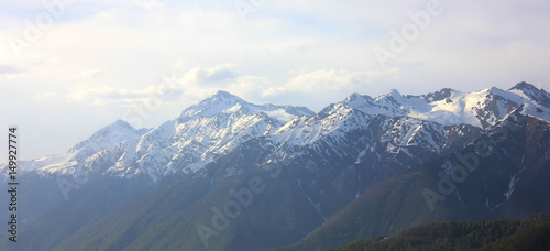 Mountain landscape background. Mountain ridge with snowy peaks in fog, cloudy sky.