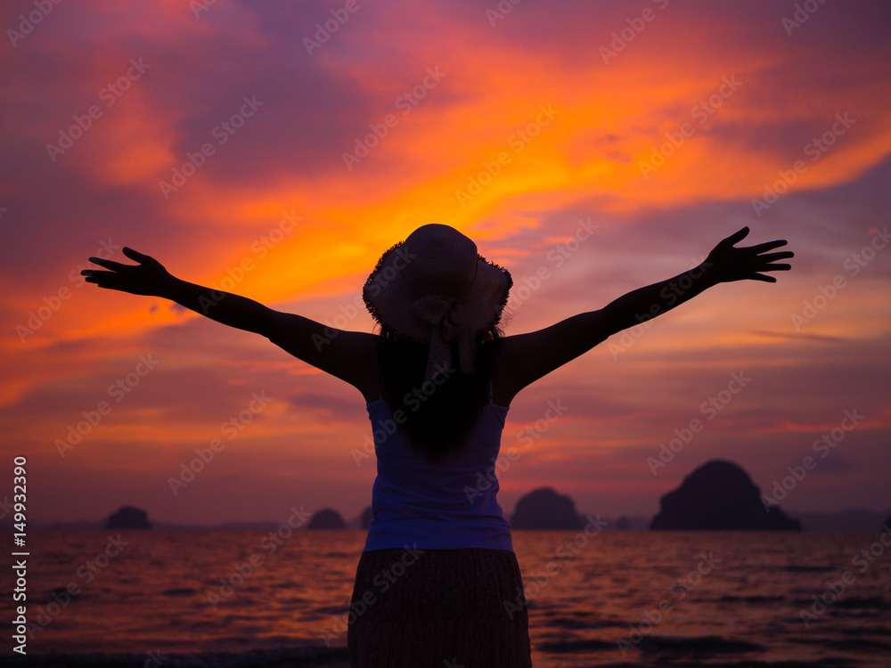 Silhouette of woman wearing hat with open arms under the sunrise near the sea