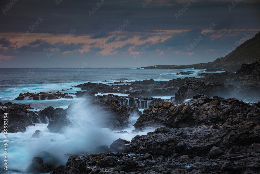 Rocky coastline with splashes of breaking waves at sunset time