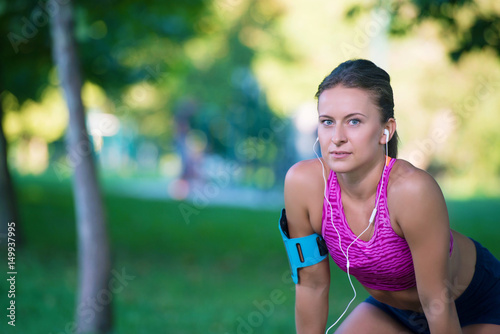 Young female runner is having break and listening to music during the run in city on a quay