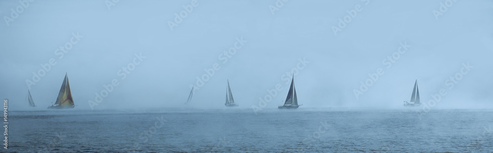 Sailing yachts floating in the foggy sea