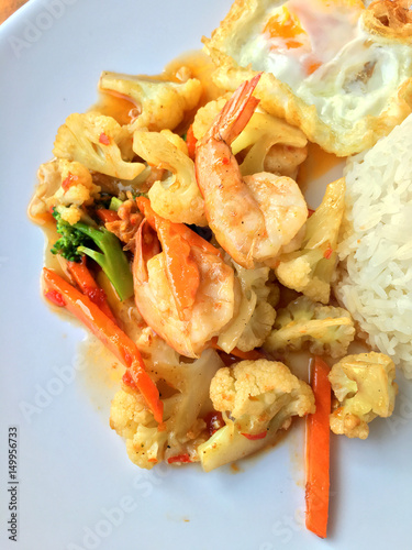 stir-fry vegetables with bean curd and shrimp in white dish with rice and fried egg on wooden background. Thai style Food.