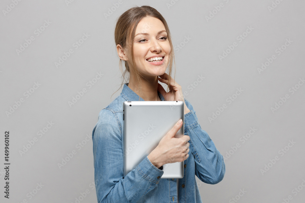 Portrait of beautiful young caucasian woman, holding tablet, laughing, while posing against grey background. Attractive european female with ebook Portrait of beautiful young caucasian woman, holding tablet, laughing, while posing against grey background. Attractive european female with ebook
