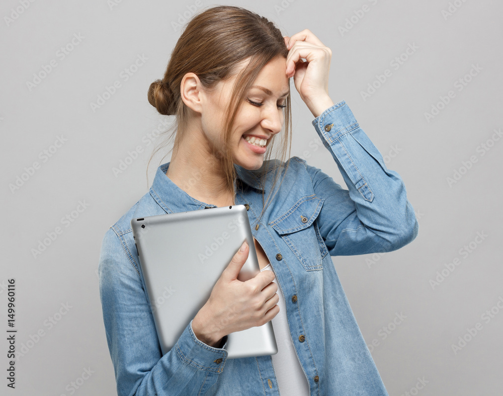 Φωτογραφία Horizontal photo of shy attractive lady isolated on grey background smiling positively and holding tablet computer close to her bosom thinking and dreaming of favorable moments and ideas, laughing