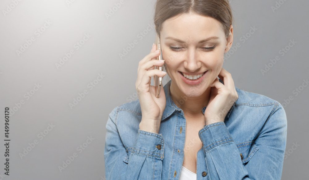 Φωτογραφία Indoor closeup with beautiful European lady in right side of picture isolated on gray background talking on smartphone with happy smile and looking down timidly, listening to her interlocutor