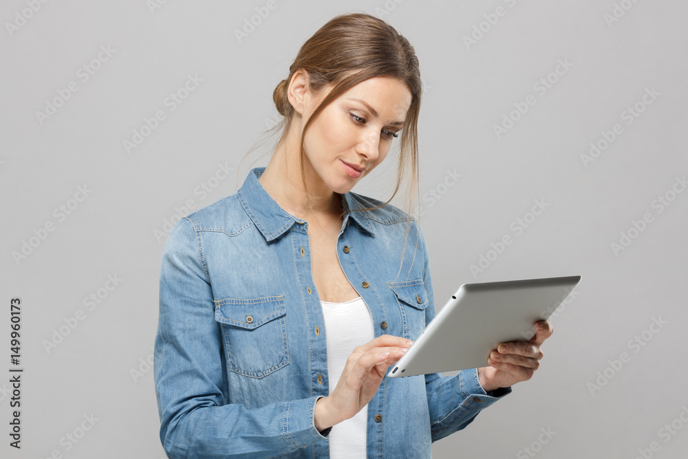 Closeup portrait of happy young woman using tablet pc isolated on grey background. Side view of a smiling female holding a digital tablet computer. Closeup portrait of happy young woman using tablet pc isolated on grey background. Side view of a smiling female holding a digital tablet computer.